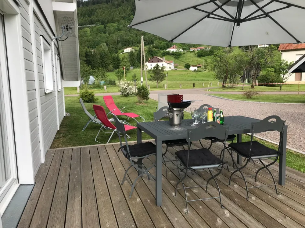 La terrasse en bois orientée plein sud  avec  salon de jardin - fauteuils détente - Parasol - barbecue