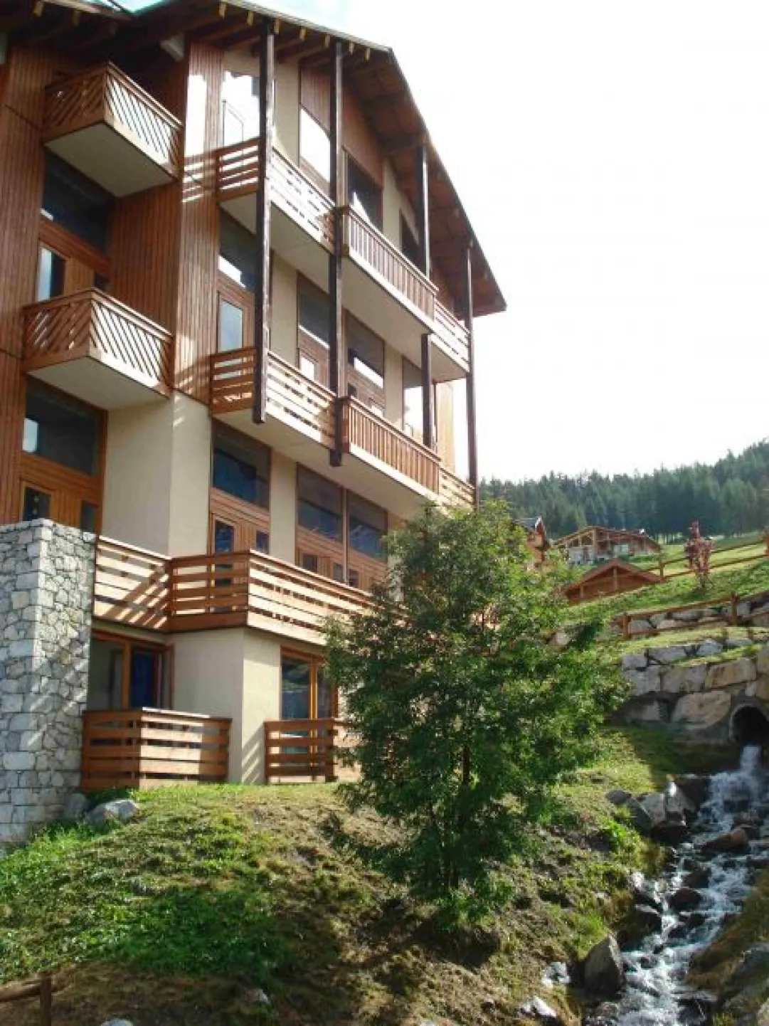 Vue de la résidence en été, avec le petit ruisseau ; l'appartement est le balcon du milieu, en haut.