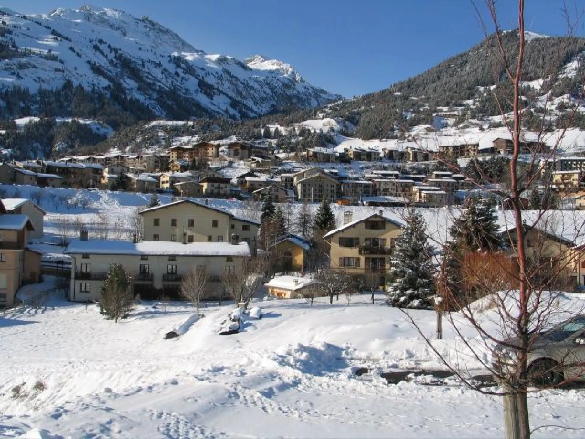 Appartement au toit blanc en premier plan devant le jardin,au fond à gauche domaine skiable.