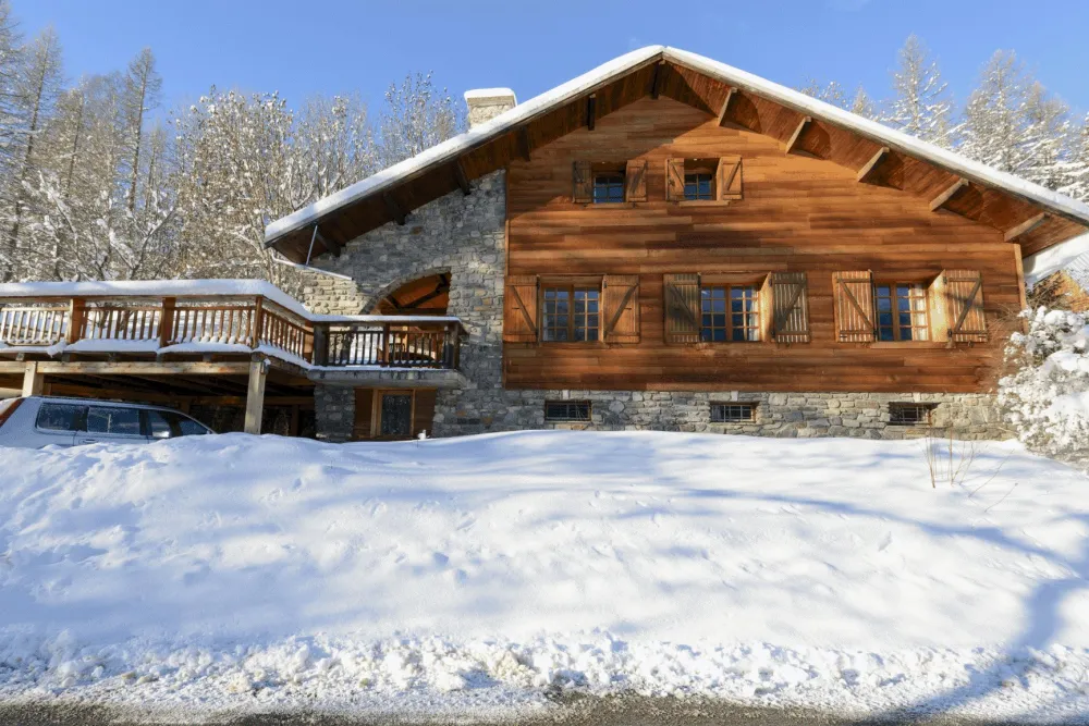 halet Mont Milo sous la neige, 160 m² en pierre et bois à Pramorel, à 5 minutes des pistes de Serre Chevalier Vallée. Terrasse extérieure face à la montagne, cadre calme en lisière de forêt, pensé pour rassembler famille et amis.